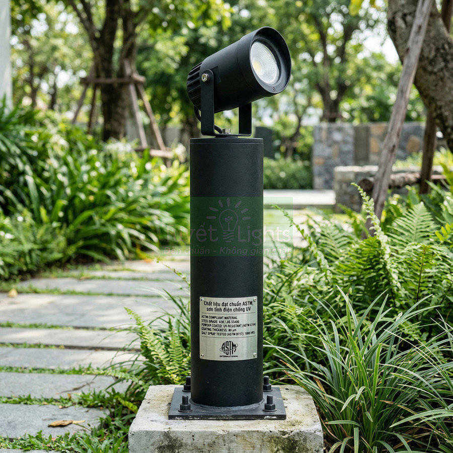 Đèn trụ sân vườn LED màu đen lắp ngoài trời trên bệ bê tông giữa cây xanh